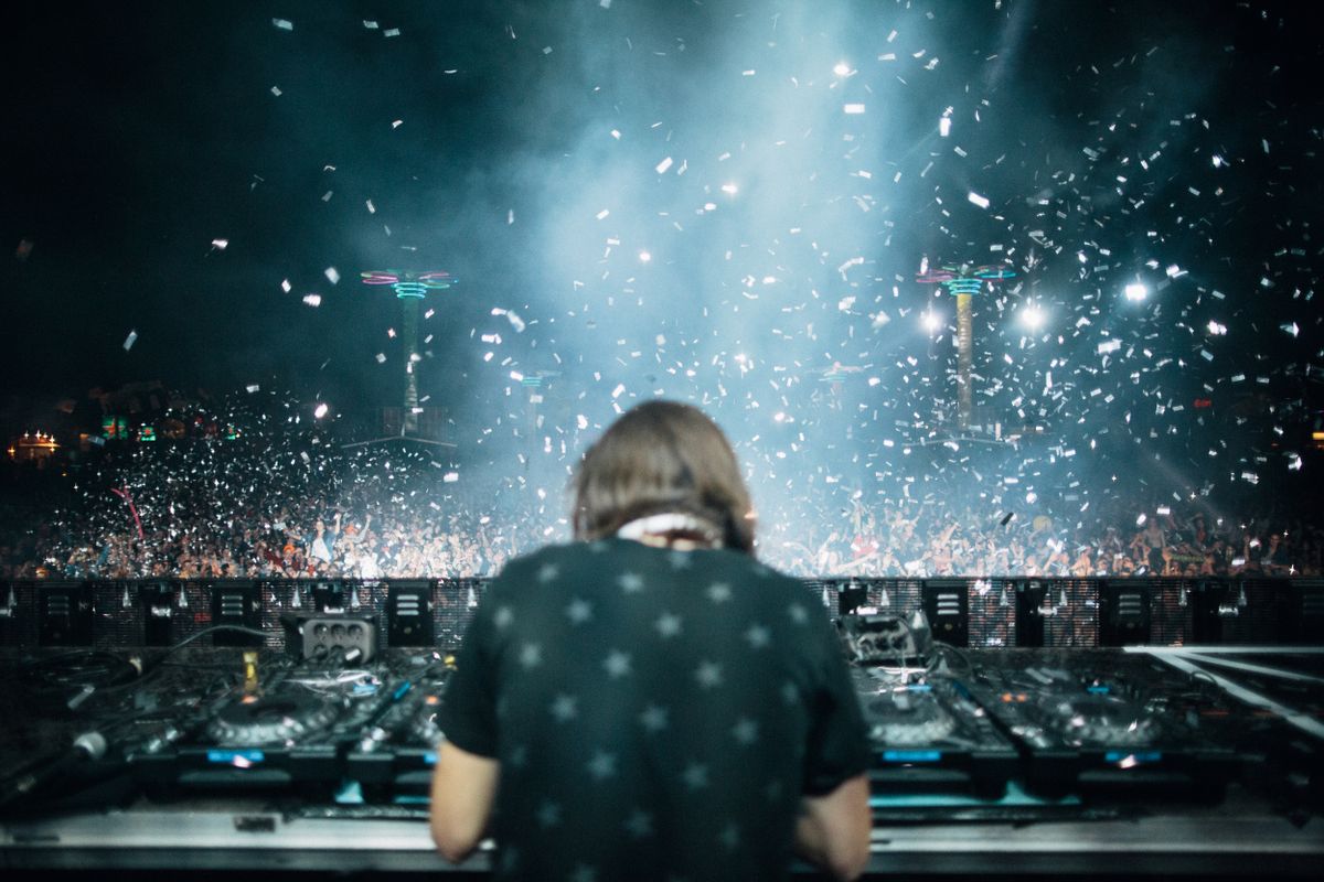 A DJ and dancing festival crowd under blue lights and confetti